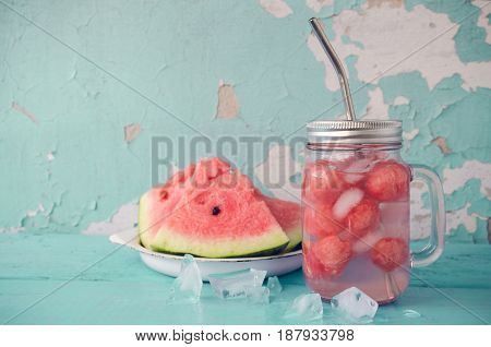 Watermelon drink in glass mason jar with slices of watermelon and ice on blue background with place for text. Summer fresh fruit flavored infused detox water. Copy space.