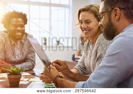 Successful business people discussing while using digital tablet in office. Multiethnic business team working on tablet in their company. Mature businessman showing data on screen to smiling woman.