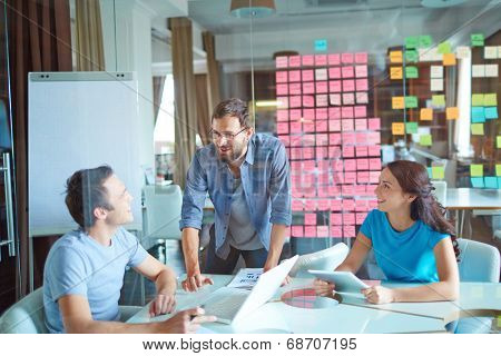 Group of three successful business partners in casual communicating at meeting in office