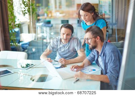 Group of three successful business partners in casual using laptop at meeting in office