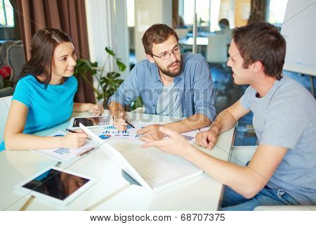 Group of three successful business partners in casual discussing ideas at meeting in office