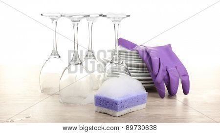 Dishes in foam with gloves and wisp on table isolated on white