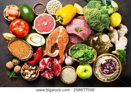 Balanced diet food background. Organic food for healthy nutrition superfoods. Meat fish legumes nuts seeds greens oil and vegetables. Top view on dark stone table.