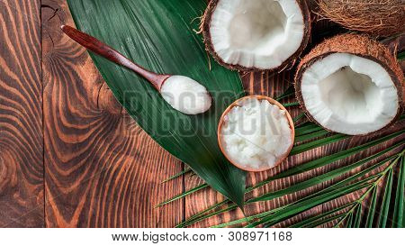 Top View Of Coconut Mct Oil In Bowl And In Spoon And Halved Coco-nut On Wooden Table. Health Benefit