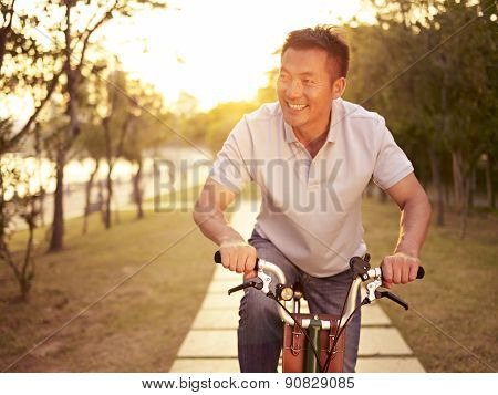 Asian Man Enjoying Bike Ride Outdoors At Sunset In Park