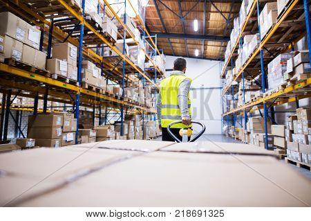 Young male warehouse worker pulling a pallet truck with boxes.