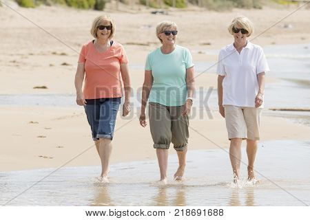 lovely group of three senior mature retired women on their 60s having fun enjoying together happy walking on the beach smiling playful in female friendship and girlfriends on holidays concept