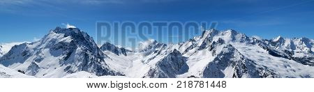 Panoramic view of snow-capped mountain peaks with mount Dombay-Ulgen and beautiful blue sky with clouds at sun windy day. Caucasus Mountains in winter region Dombay.