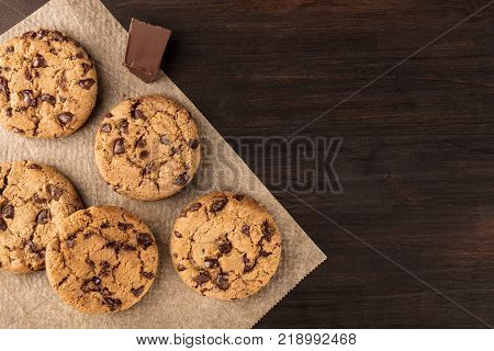 An overhead photo of chocolate chips cookies with a slice of chocolate, shot from above on a piece of baking paper, with copy space