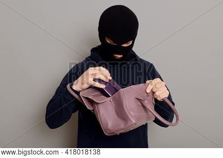 Young Male Burglar Steals Woman's Handbag, Opens Bag And Looking Inside, Pulls Out Wallet, Wearing B