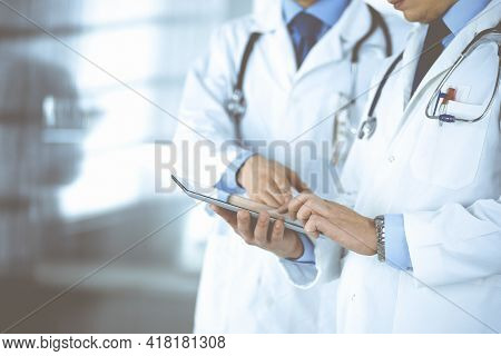 Group Of Unknown Doctors Use A Computer Tablet To Check Up Some Medical Names Records, While Standin