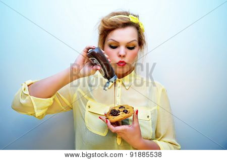 Trendy young woman is pouring chocolate sauce over chocolate chip cookie.