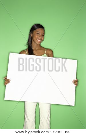 Portret van Afro-Amerikaanse tiener meisje bedrijf leeg wit bord staande tegen groene rug glimlachen