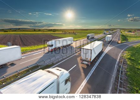 Many delivery trucks driving through agricultural fields. Fast blurred motion drive on the freeway at beautiful sunny day. Freight scene on the motorway near Belgrade Serbia.