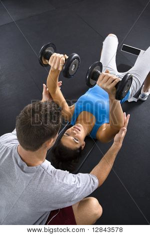 Man assisting woman lifting weights at gym.