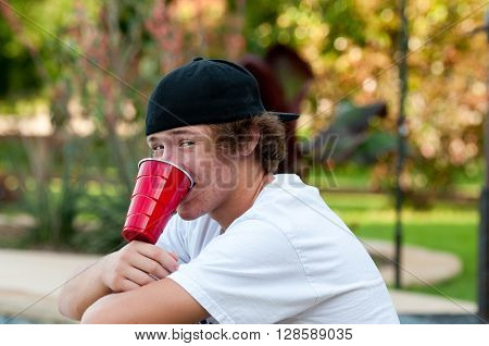 Teen boy outdoors with acne looking at camera with black backwards hat and white shirt.