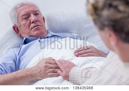 Close-up of a dying elderly man in a hospital bed holding his wife's hand