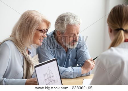 Older Couple Reading Contract At Meeting With Real Estate Agent Considering New Home Purchase, Realt