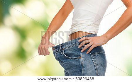 healthcare, diet and fitness concept - close up of female showing big jeans