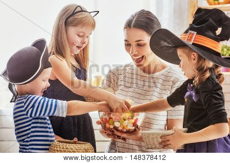 Happy family celebrating Halloween! Young mom treats children with candy. Funny kids in carnival costumes.