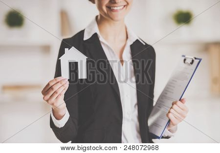 Smiling Realtor Holding Tablet And Paper Model Of House. Real Estate Sales Concept. Getting Access T