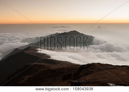 Picturesque Landscape Of Mountain Valley Filled With Curly Clouds At Sunrise. Dramatic Hill Lit Up B