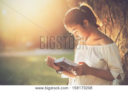 Asian girl reading book at park in summer sunset light. asian woman reading book in Thailand. asian Beautiful woman reading a book at big tree.