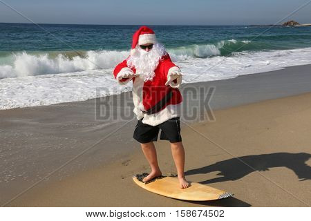 Surfing Santa. Santa Claus Surfs on his Surf Board while on a Beautiful Beach with a Blue Ocean. Focus on Santas Face Santa Vacation. Surfing Santa. Santa goes Surfing. Santa Claus enjoys the beach 

