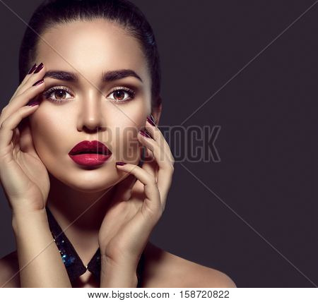 Beauty Brunette Woman with Perfect Makeup. Beautiful Professional Holiday Make-up. Red Lips and Nails, perfect eyebrows. Beauty Girl's Face isolated on dark background