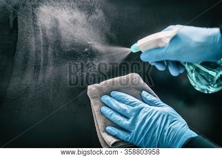 Surface home cleaning spraying antibacterial sanitizing spray bottle disinfecting against COVID-19 spreading wearing medical blue gloves. Sanitize surfaces prevention in hospitals and public spaces.