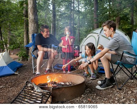 father camping with kids while kids roast marshmallows