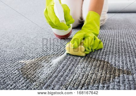 Close-up Of Person Hand Wearing Gloves Spraying Detergent On Grey Carpet To Remove Stains