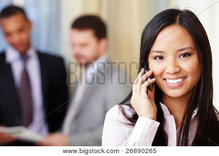 Portrait of young happy asian woman on phone with her business partners on the background