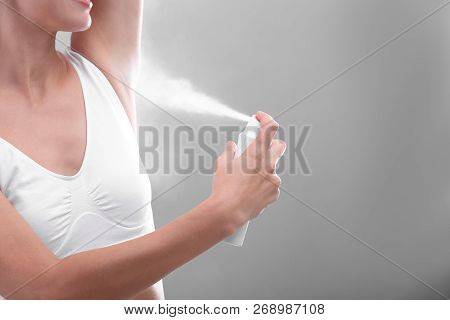 Young Woman Using Deodorant On Grey Background, Closeup. Space For Text