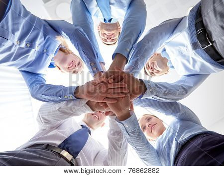 business, people and teamwork concept - smiling group of businesspeople standing in circle and putting hands on top of each other