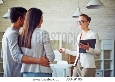 Female broker consulting young couple in realtor office