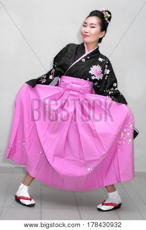 A funny geisha in a kimono fools around lifting her skirt and clapping her feet.