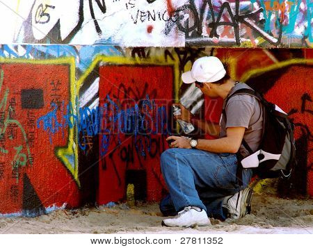 Young man painting graffiti on n ever changing public tag wall. It is painted new daily