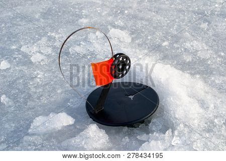 Winter Imitation Fish For Predatory Fish. The Imitation Fish Is Round With A Red Flag On The Ice.