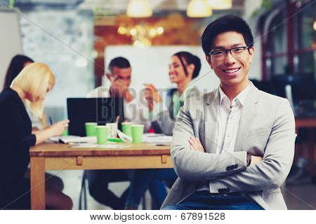 Portrait of cheerful businessman with arms folded sitting in front of colleagues