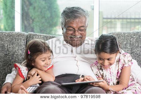 Modern technology concept. Grandparent and grandchildren using touch screen tablet computer. Portrait Indian family at home. Asian people living lifestyle.