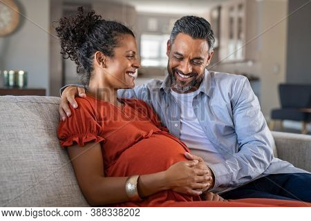 Mid adult couple expecting a baby while husband caresses the belly of his pregnant african woman. Lovely indian man touching belly of his girlfriend and feeling baby movement.