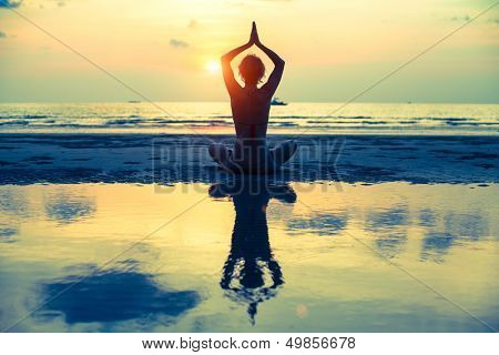 Yoga vrouw in lotus pose zittend op het strand tijdens zonsondergang, met weerspiegeling in water (kruis-proces