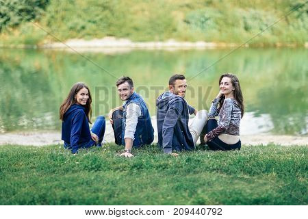 Two Couples Sitting On Grass By River Turned Looking Camera