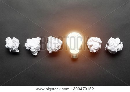 Lightbulb And Crumpled White Paper Balls On Black Background. Successful Solution Of Problem. Think 