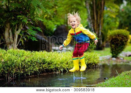 Child Playing In Puddle. Kids Jump In Autumn Rain