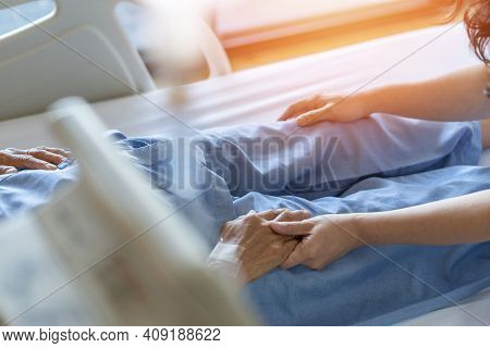 Caregiver And Elderly Senior Patient (aged Old Adult Person) Holding Hands In Hospital Bed Or Nursin