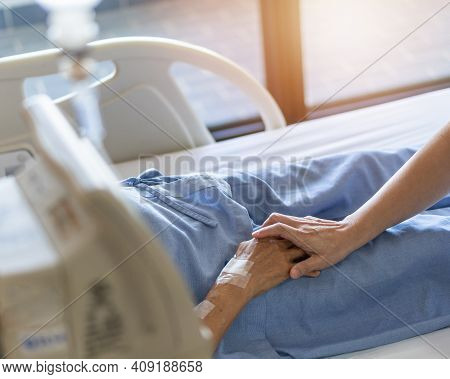 Caregiver And Elderly Senior Patient (aged Old Adult Person) Holding Hands In Hospital Bed Or Nursin