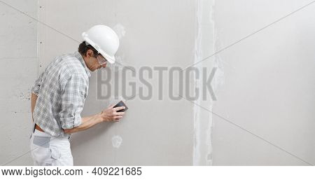 Man Drywall Worker Or Plasterer Sanding And Smoothing A Plasterboard Walls With Stucco Using A Sandp