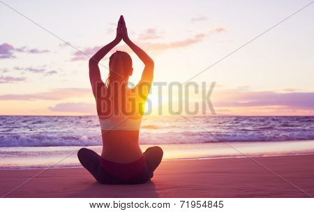 Young healthy woman practicing yoga on the beach at sunset